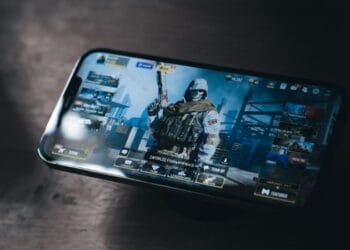 a person holding a cell phone with a video game on the screen - Graphite iPhone Pro Max with the Call of Duty: Mobile video game by Activision on screen. With a dark gradient dramatic light to it., tags: vague de tricheurs - unsplash