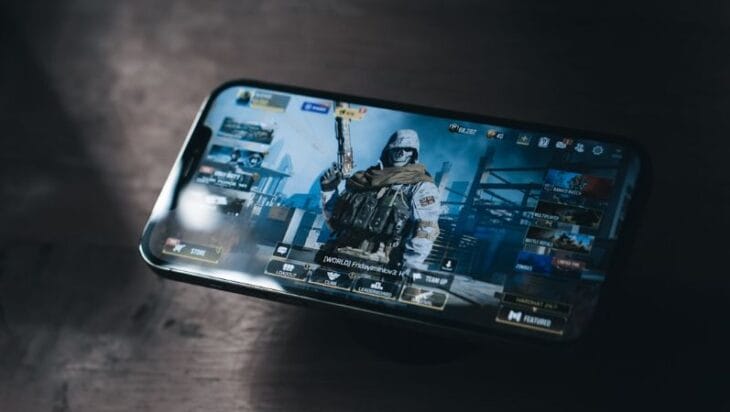 a person holding a cell phone with a video game on the screen - Graphite iPhone Pro Max with the Call of Duty: Mobile video game by Activision on screen. With a dark gradient dramatic light to it., tags: vague de tricheurs - unsplash